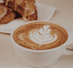 Cup of coffee with coffee art on it and a plate of pastries on the side