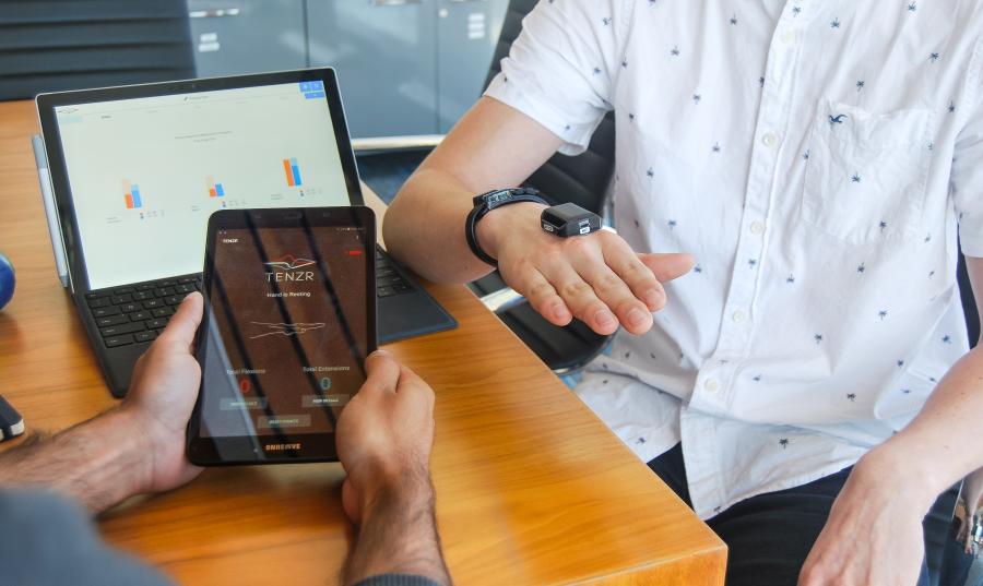 Person holding a tablet with health-related app open while other person has sensor on their hand
